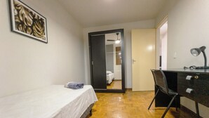 Quarto com cama, escrivaninha e cadeira. Há uma porta que dá para um banheiro.