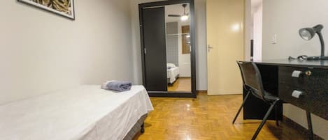 A room with a bed, a desk, and a chair. There is a door leading to another room.