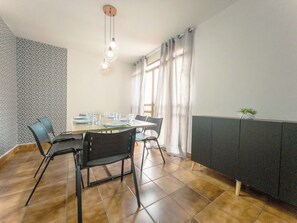 Een eethoek met een tafel voor vier personen, stoelen, een hangende lamp en een raam met gordijnen.