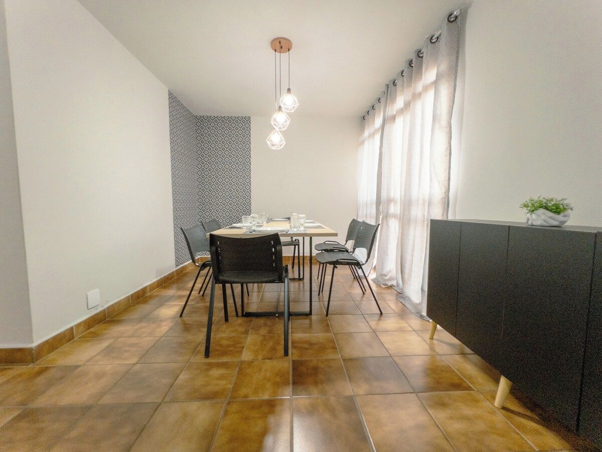 Een eethoek met een tafel, stoelen, een hanglamp en een radiator.