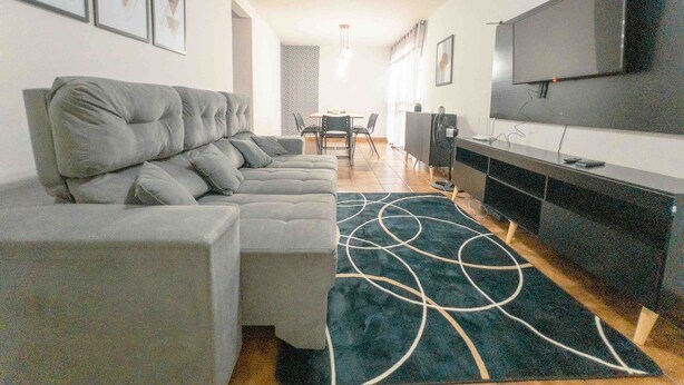 Uma sala de estar moderna com um sofá seccional, uma televisão de tela plana e um tapete estampado.