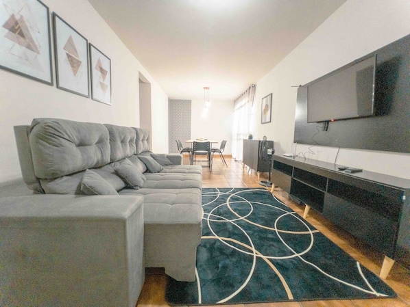 Een moderne woonkamer met een hoekbank, een flatscreen televisie en een kamerbreed tapijt met een patroon.