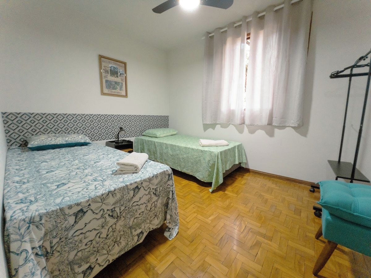 Una stanza con due letti, una ventola a soffitto, una finestra con tende e un pavimento in legno.