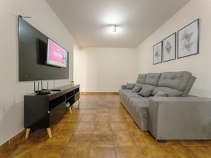 Een woonkamer met een grijze bank, een flatscreen televisie aan de wand en een zwarte tv-kast.