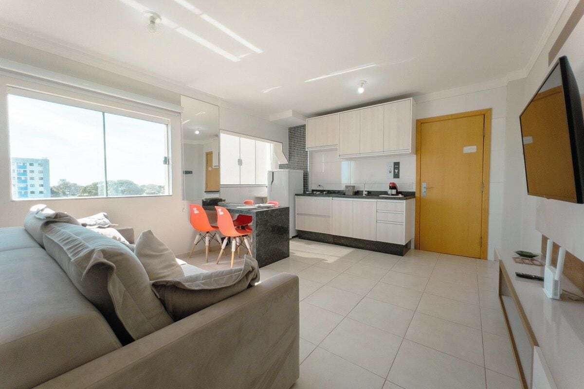 Una sala de estar moderna con un sofá y sillones, un comedor con mesa y sillas, una cocina con armarios y electrodomésticos, y un amplio ventanal con vistas a la ciudad.