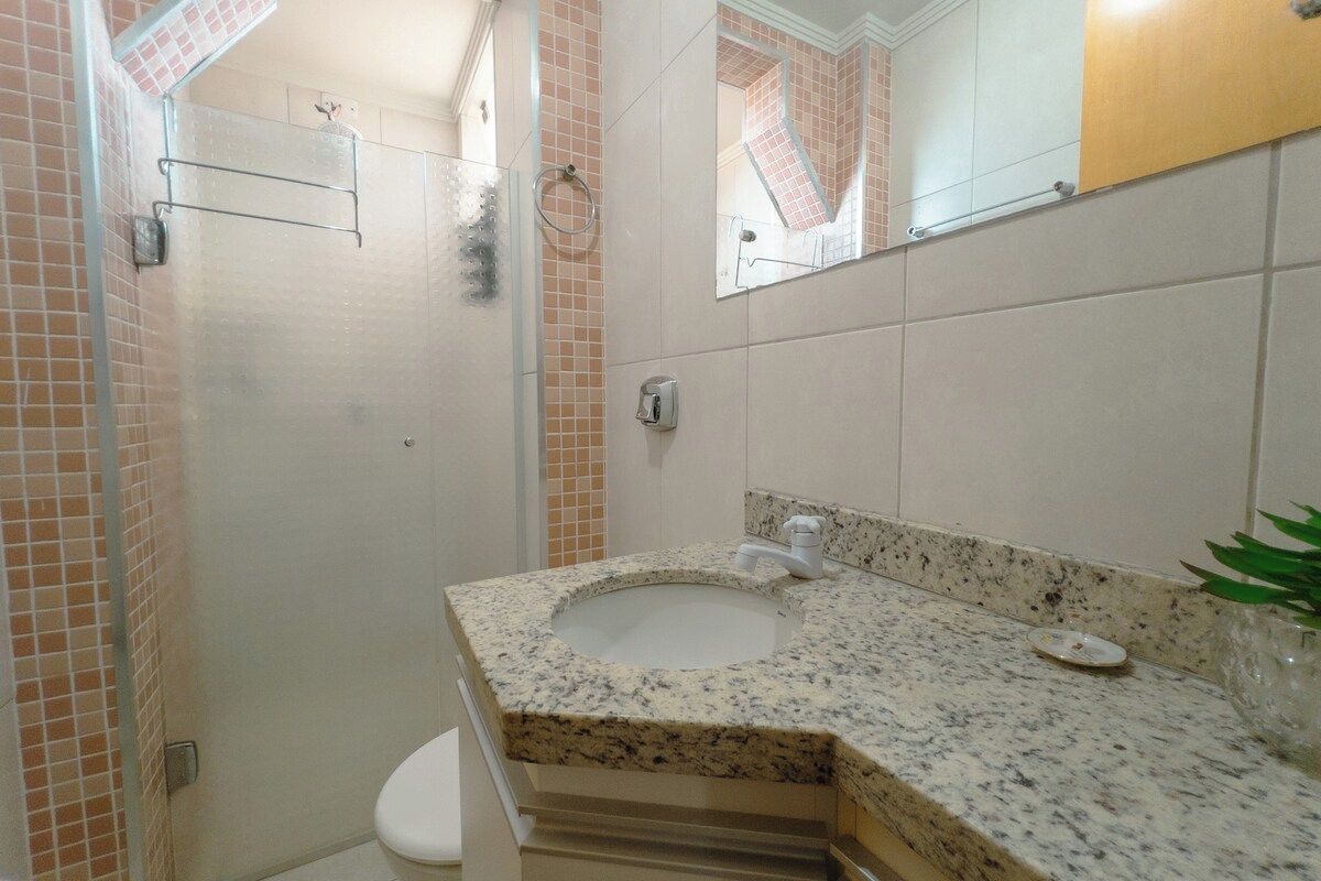 Un baño con lavamanos de encimera de granito, un espejo y zona de ducha.