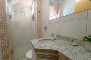 Een badkamer met een wastafel met granieten blad, een spiegel en een douche.