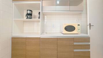 A compact kitchenette with a coffee maker, microwave, and wooden cabinets.