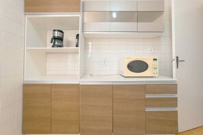 Uma cozinha compacta equipada com cafeteira, micro-ondas e armários de madeira.