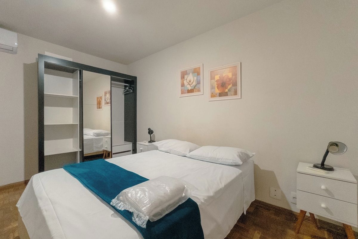 A hotel room with a bed, a wardrobe, a bedside table, and two framed pictures on the wall.