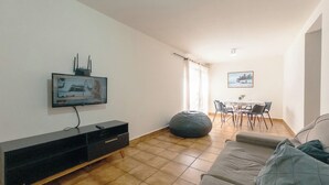 A living room with a flat-screen TV mounted on the wall, a sofa, a bean bag, a dining table with chairs, and a window with curtains. - Spacious Apartment beside Parque do Inga - MC31 (Maringá)