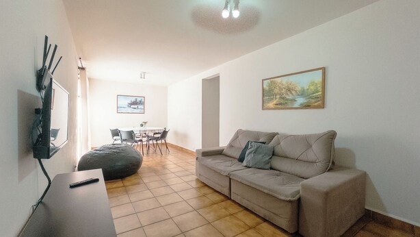 A living room with a sofa, a coffee table, and a TV. There is a painting on the wall and a ceiling light fixture. - Spacious Apartment beside Parque do Inga - MC31 (Maringá)