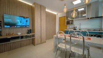 A modern kitchen with a built-in TV, dining area with chairs, and pendant lights.