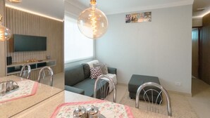 A modern living room with a sofa, a dining table with a placemat, and a television mounted on the wall. - Modern Apartment in Zona 7 Maringa - MN704 (Maringá)