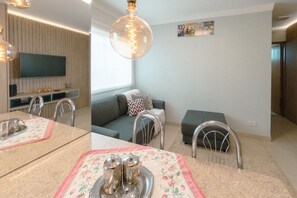 Ein modernes Wohnzimmer mit einer Couch, einem Esstisch mit Unterlage und einem an der Wand montierten Fernseher.