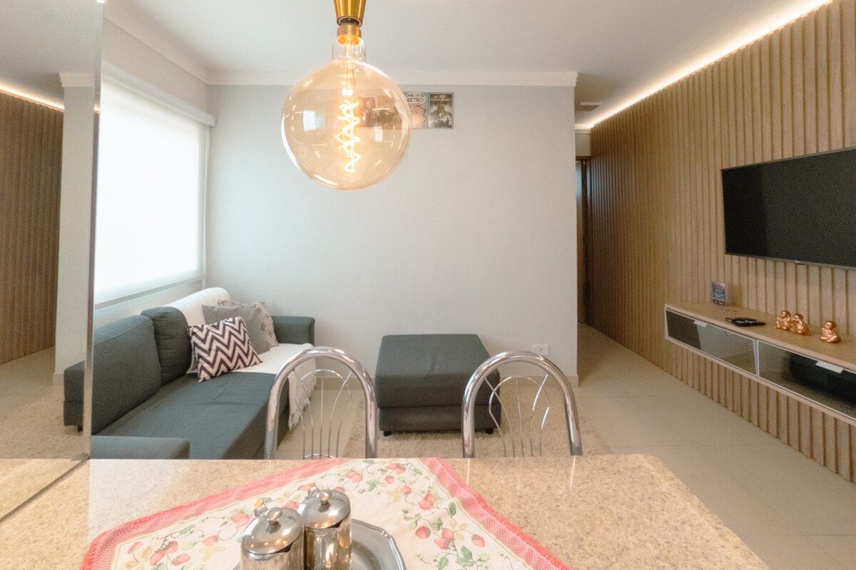 A modern living room with a sofa, chairs, a TV, and a decorative light fixture.