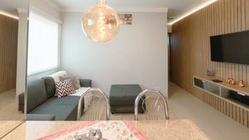 A modern living room with a sofa, chairs, a TV, and a decorative light fixture.