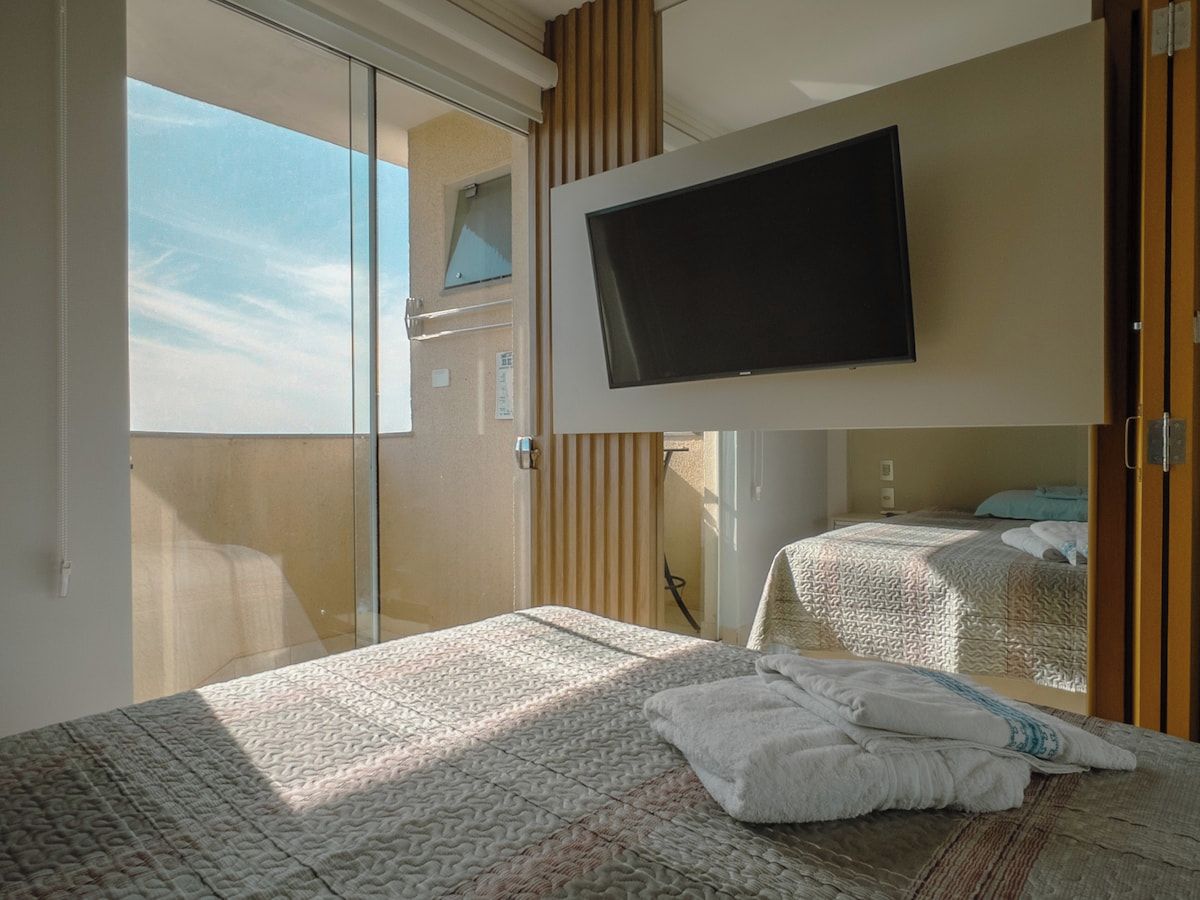 A hotel room with a bed, a television mounted on the wall, and a sliding door leading to a balcony.