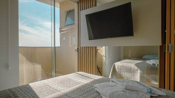A hotel room with a bed, a television mounted on the wall, and a sliding door leading to a balcony.