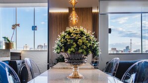 A modern conference room with a glass table, chairs, a decorative vase with flowers, and a city view through large windows. - Modern Apartment in Zona 7 Maringa - MN704 (Maringá)