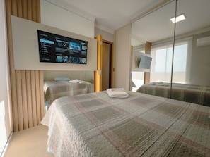 Ein Hotelzimmer mit einem großen Bett, einem an der Wand befestigten Fernseher und einem Spiegel, der den Raum reflektiert.