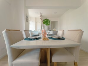 A dining area with a white table, four chairs, and a decorative plant centerpiece. - Two-Bedroom Apartment near the Cathedral - RC1102 (Maringá)