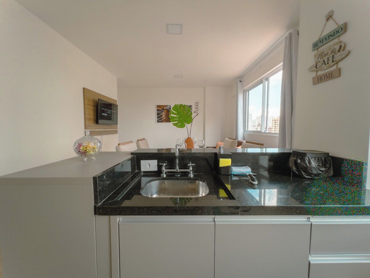 Una cocina moderna con encimera negra, pileta de acero inoxidable y ventana que permite entrada de luz natural.