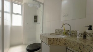 Et badeværelse med bruser, toilet, håndvask og spejl.