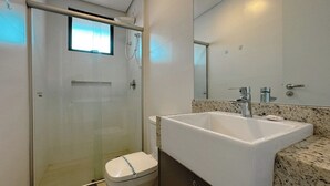 Un bany amb dutxa tancada amb vidre, un vàter blanc i un lavabo amb taulell de granit.