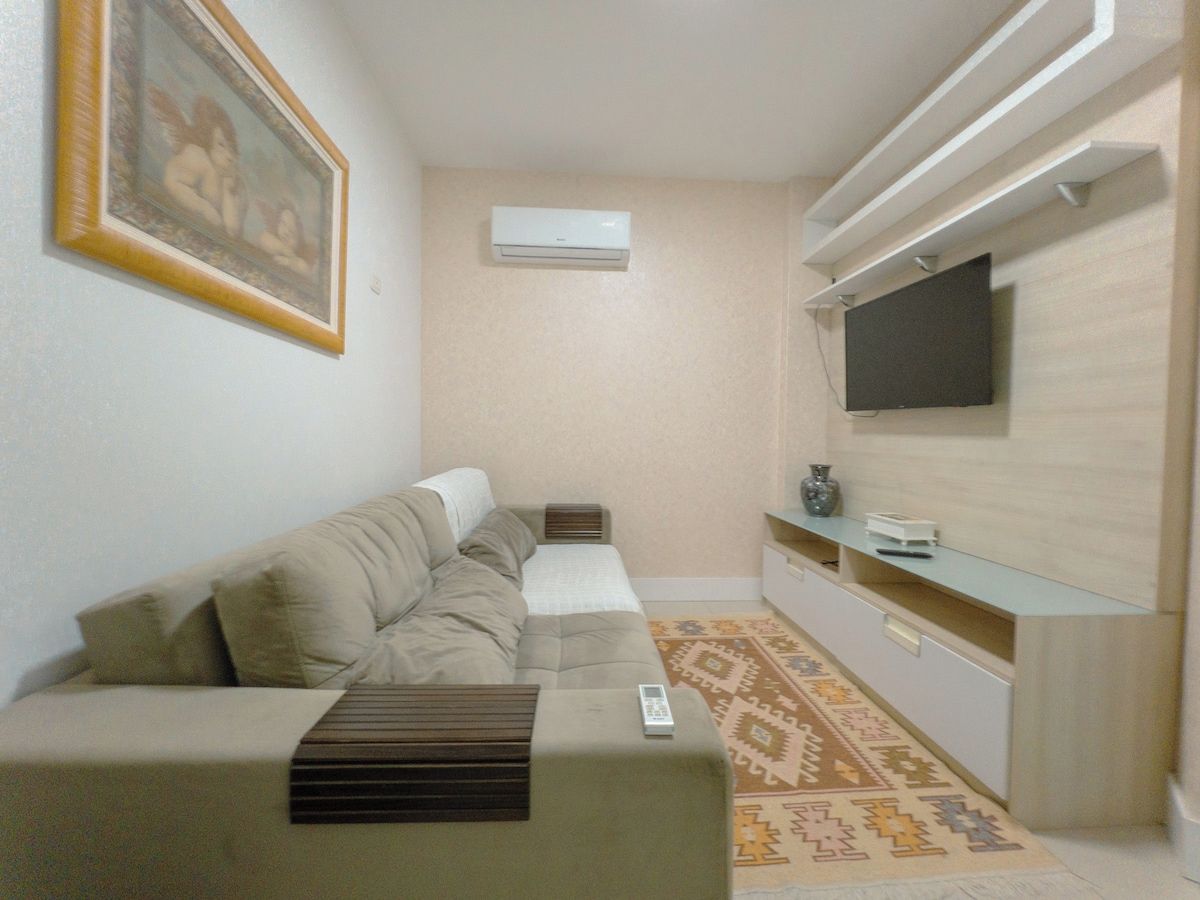 A living room with a sofa, a flat-screen TV mounted on the wall, and a small table with a vase.