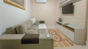 A living room with a sofa, a flat-screen TV mounted on the wall, and a small table with a vase. - Downtown Apartment next to Avenida Center - PL603 (Maringá)