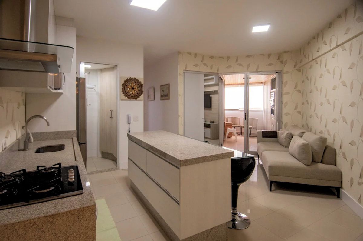 A modern kitchen with a central island, a dining area with a sofa, and a patterned wall.