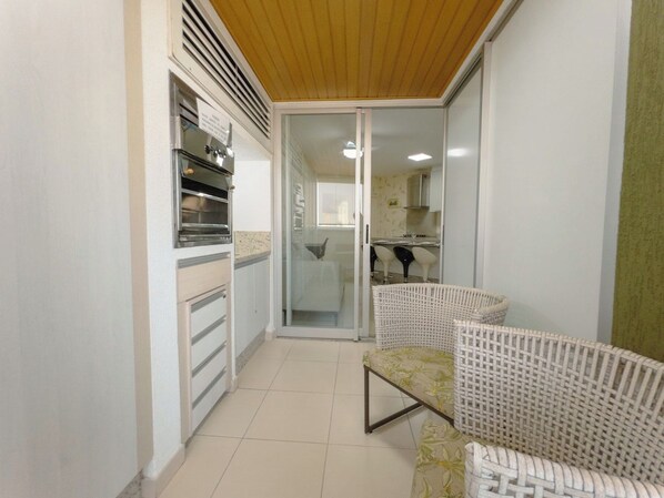 A narrow hallway with a sliding glass door leading to a kitchen area. There are wicker chairs and a small table in the hallway.