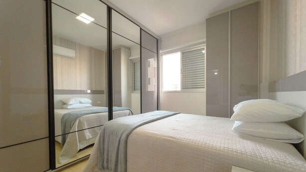 A bedroom with a bed, a bedside table, a mirror, and a wardrobe. - Downtown Apartment next to Avenida Center - PL603 (Maringá)
