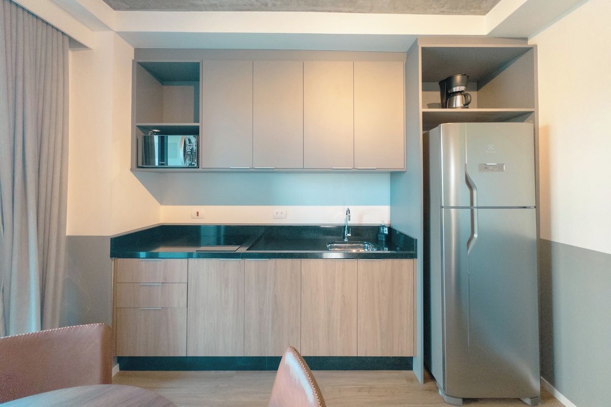 A compact kitchen with a built-in microwave, a stainless steel refrigerator, and a wooden cabinet.
