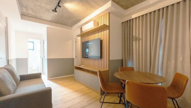 A modern interior with a wooden table and chairs, a flat-screen TV mounted on a wooden panel, and a sofa. - Comfort and Style in Zona 7 for 5 Guests - BEDEO601 (Maringá)