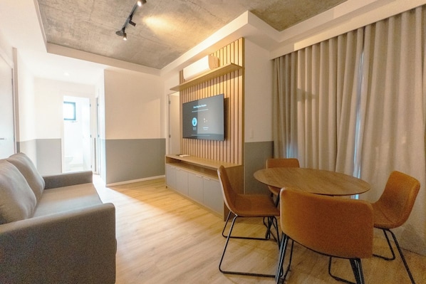 A modern interior with a wooden table and chairs, a flat-screen TV mounted on a wooden panel, and a sofa. - Comfort and Style in Zona 7 for 5 Guests - BEDEO601 (Maringá)