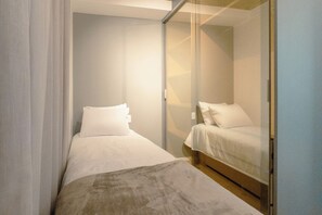 A small, modern bedroom with two beds, a glass partition, and a neutral color scheme. - Comfort and Style in Zona 7 for 5 Guests - BEDEO601 (Maringá)