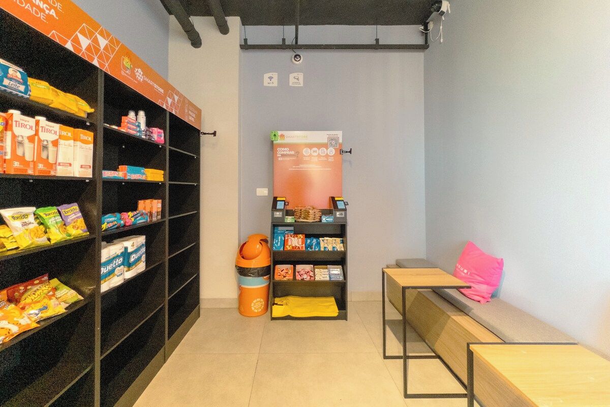 Ein kleiner Raum mit Regalen voller Snacks, einem Mülleimer, einem Tisch mit einem rosa Kissen und einem Schild an der Wand.
