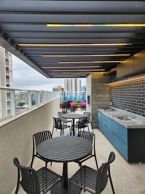 An outdoor patio with a round table and chairs, a built-in kitchen area, and a view of the cityscape. - Comfort and Style in Zona 7 for 5 Guests - BEDEO601 (Maringá)
