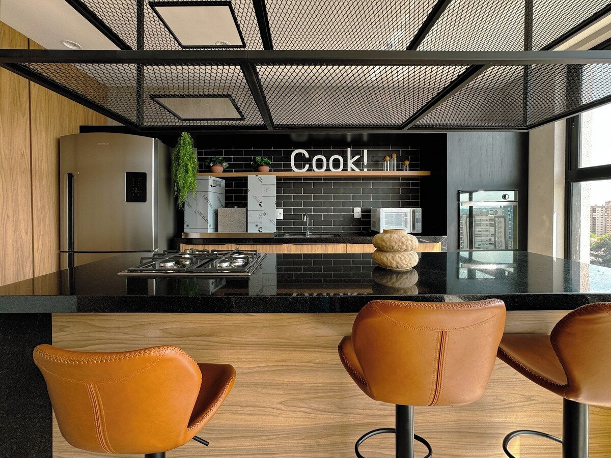 Cozinha moderna com bancada preta, eletrodomésticos de aço inoxidável e um letreiro com a inscrição 'Cook!'.