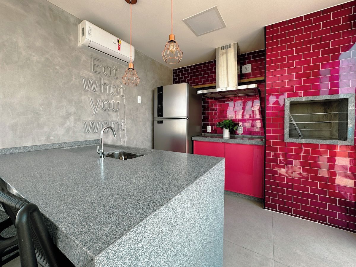 Cozinha com bancada de granito, eletrodomésticos de aço inoxidável e backsplash com azulejos vermelhos.