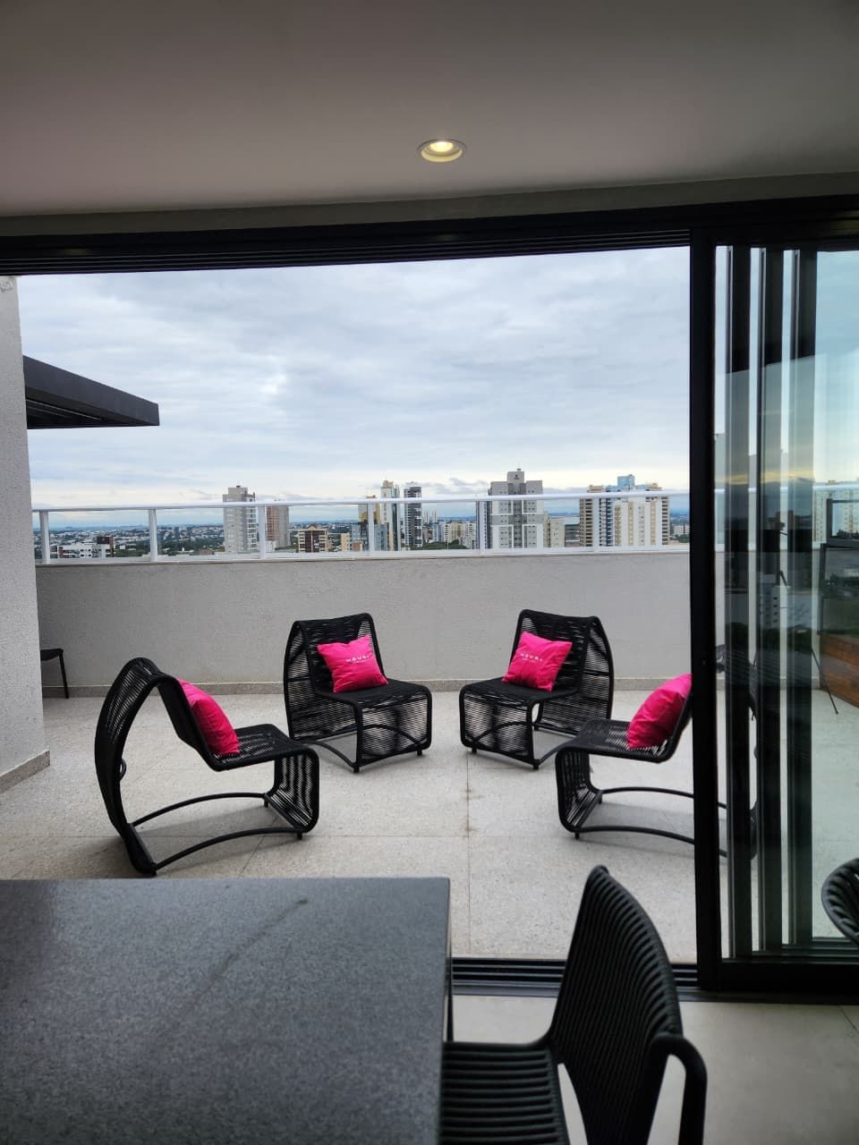 Uma varanda com mesa e cadeiras, porta de vidro e vista para a cidade.