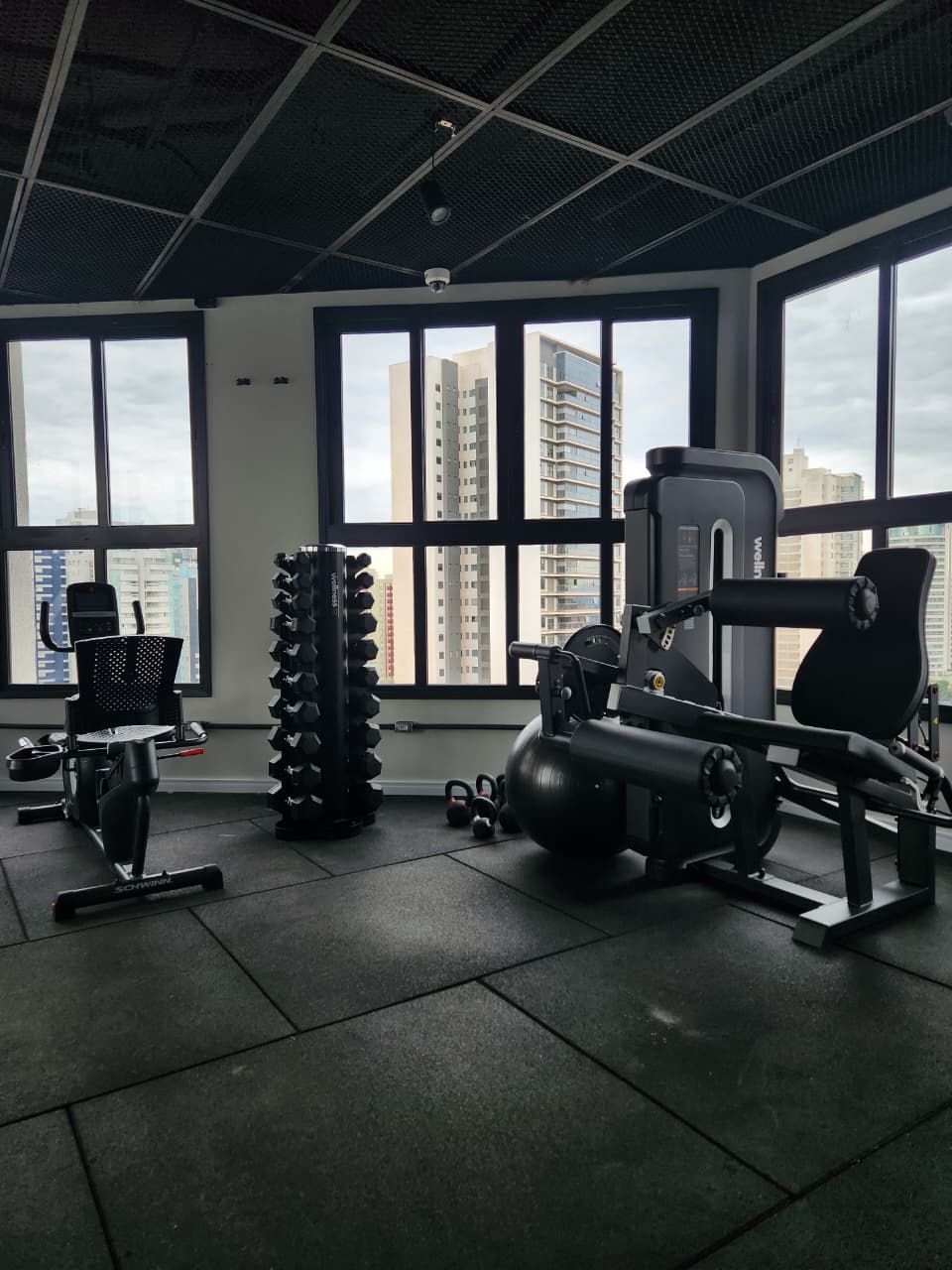 Ein Fitnessstudio mit Trainingsgeräten, großen Fenstern und Blick auf Gebäude.