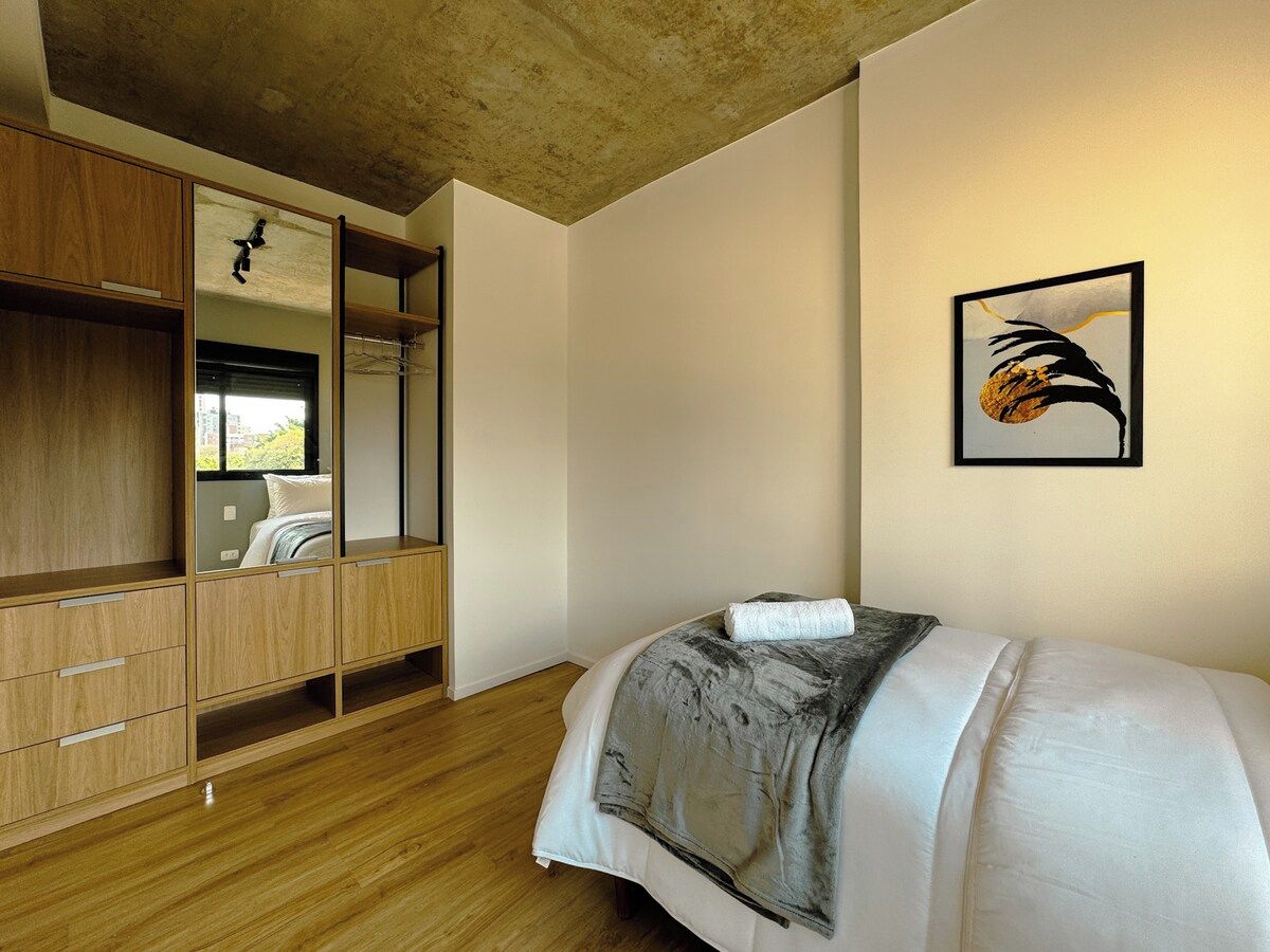 A bedroom with a bed, wooden wardrobe, and a framed picture on the wall.