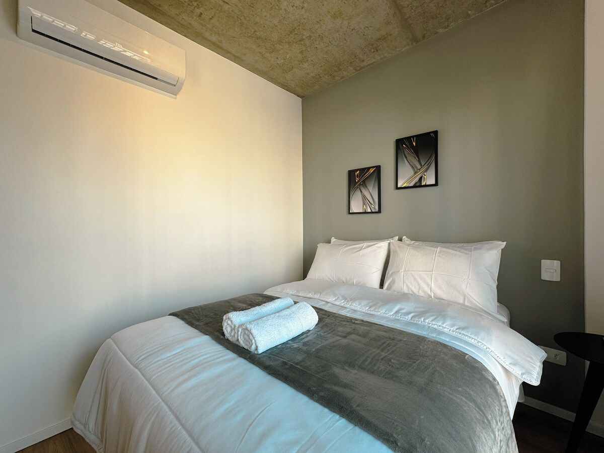 Ein Hotelzimmer mit einem Bett, einer Wandklimaanlage und zwei gerahmten Bildern an der Wand.