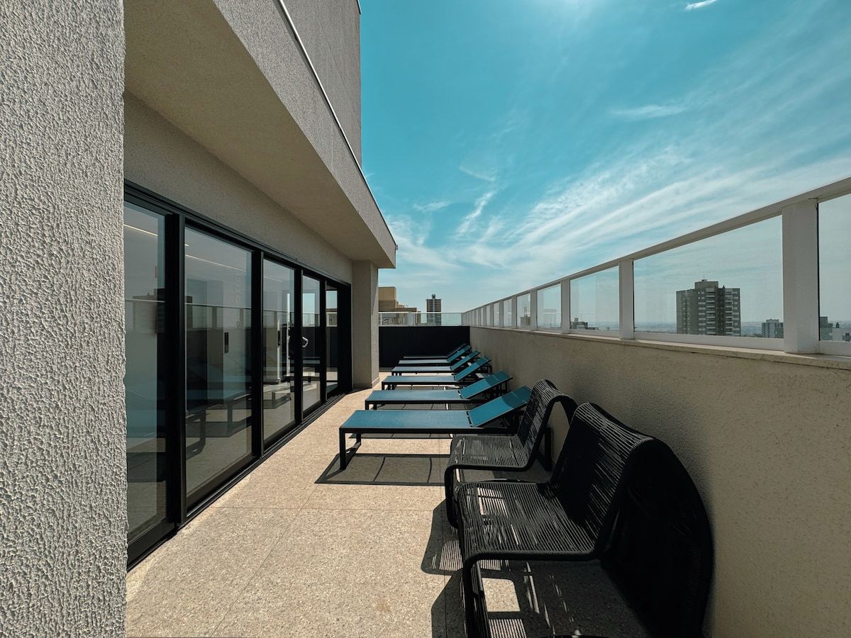 Terraza en la azotea con sillones de sol y un banco, con vistas al horizonte de la ciudad.