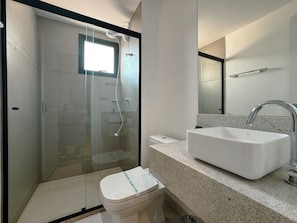 Ein modernes Badezimmer mit einer gläsernen Duschkabine, einem weißen Waschbecken und einer Toilette.