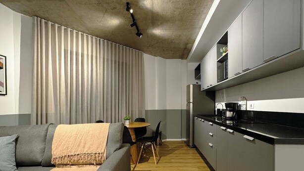 A modern kitchen with grey cabinets, a black countertop, and a dining area with a table and chairs. - Modern Apartment in New Building - BEDEO505 (Maringá)