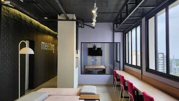 Una sala de reuniones moderna con una mesa larga, sillas rojas, un sofá y un amplio ventanal con vistas a la ciudad.